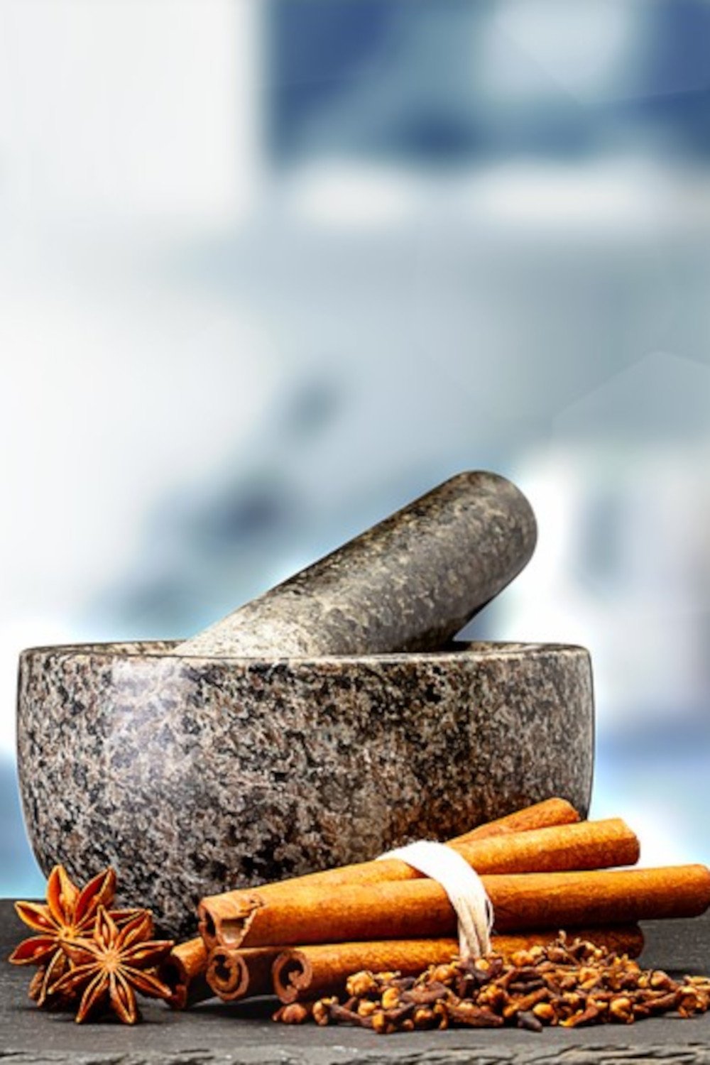 A mortar and pestle with star anise, cinnamon quills, and cloves in the foreground